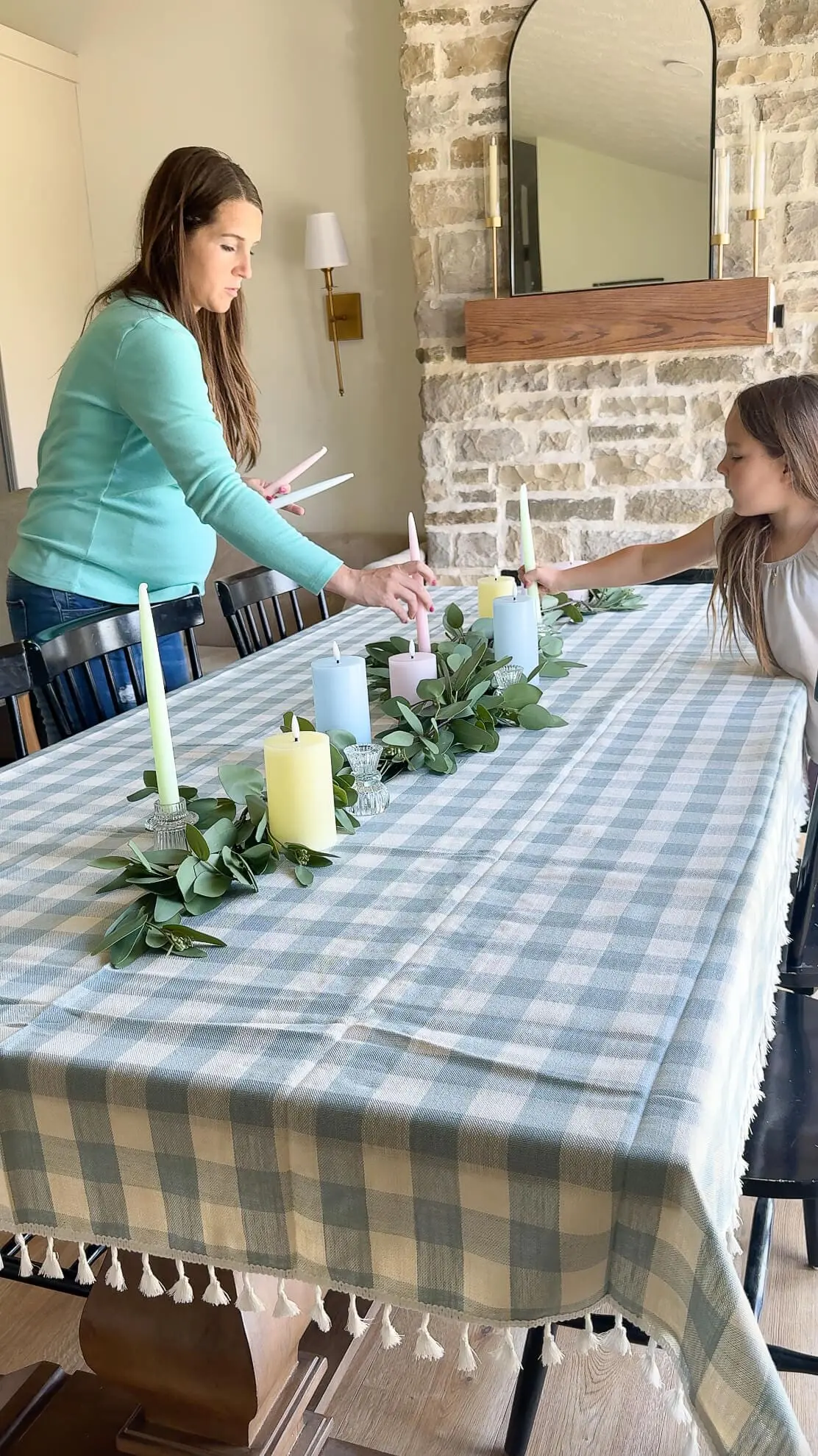 Mother and daughter setting pastel Easter candles on a eucalyptus garland centerpiece for Easter table decor.